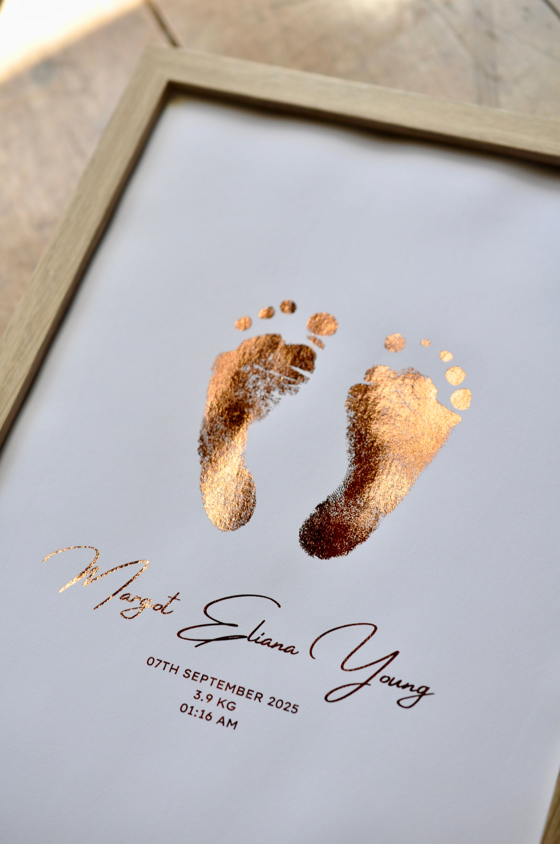 Framed artwork with gold baby footprints and personalized text on a white background