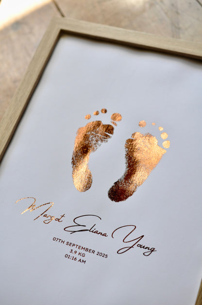 Framed artwork with gold baby footprints and personalized text on a white background