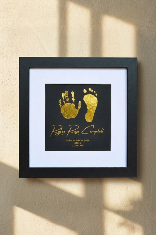 Framed gold hand and footprints with text on a beige wall