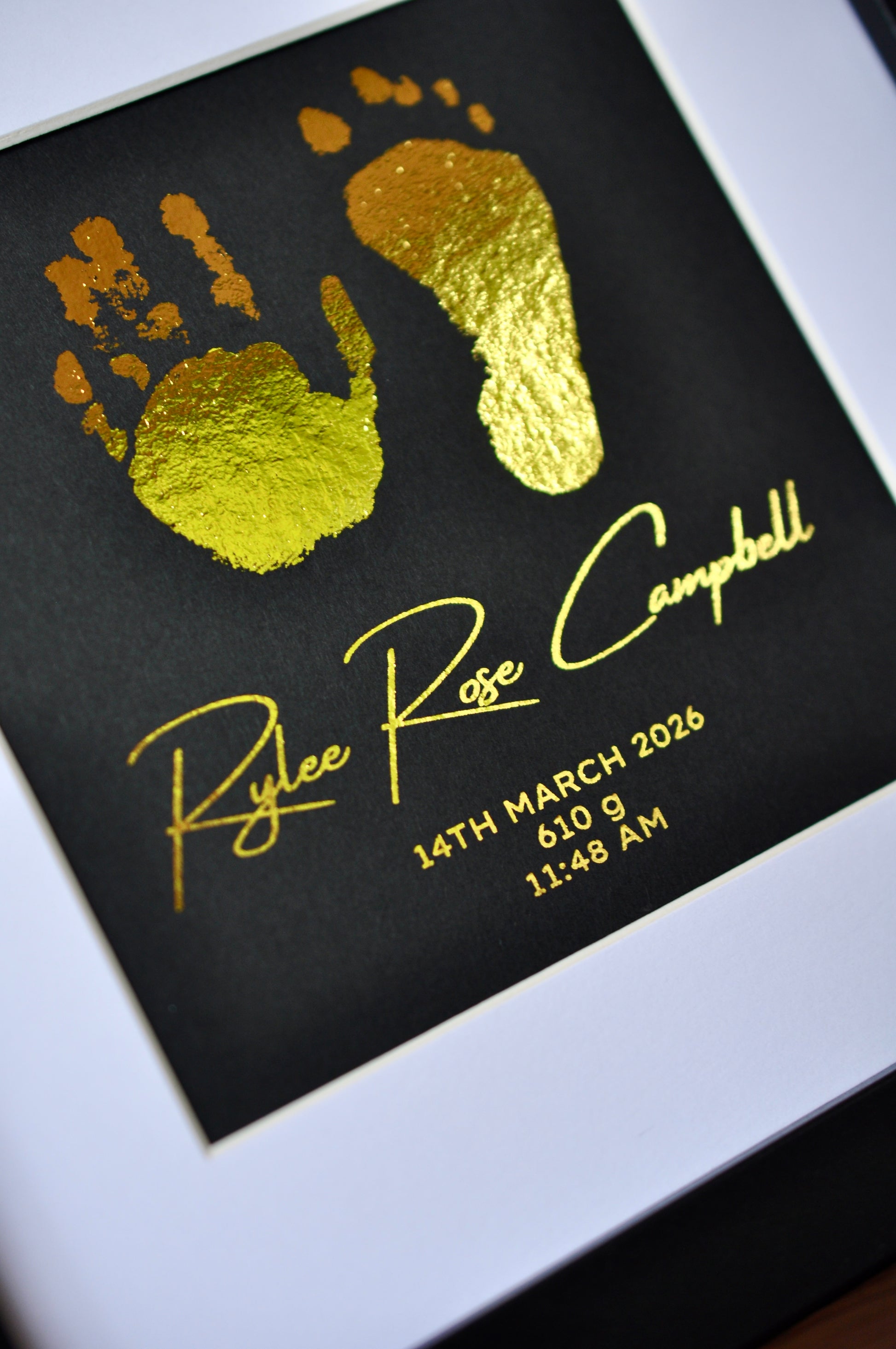 Gold hand and footprints on a black background with text, framed.