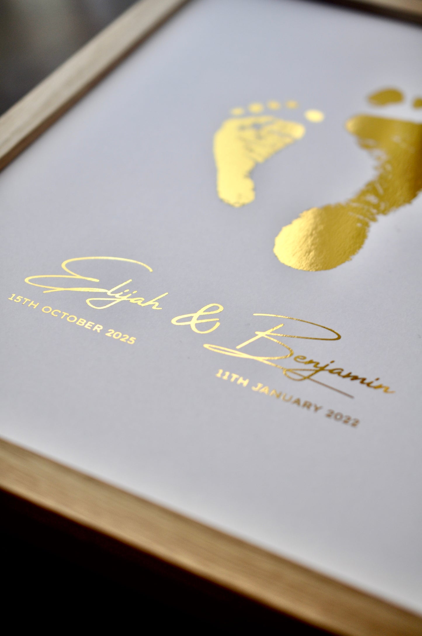 Framed print with gold footprints and names on a white background