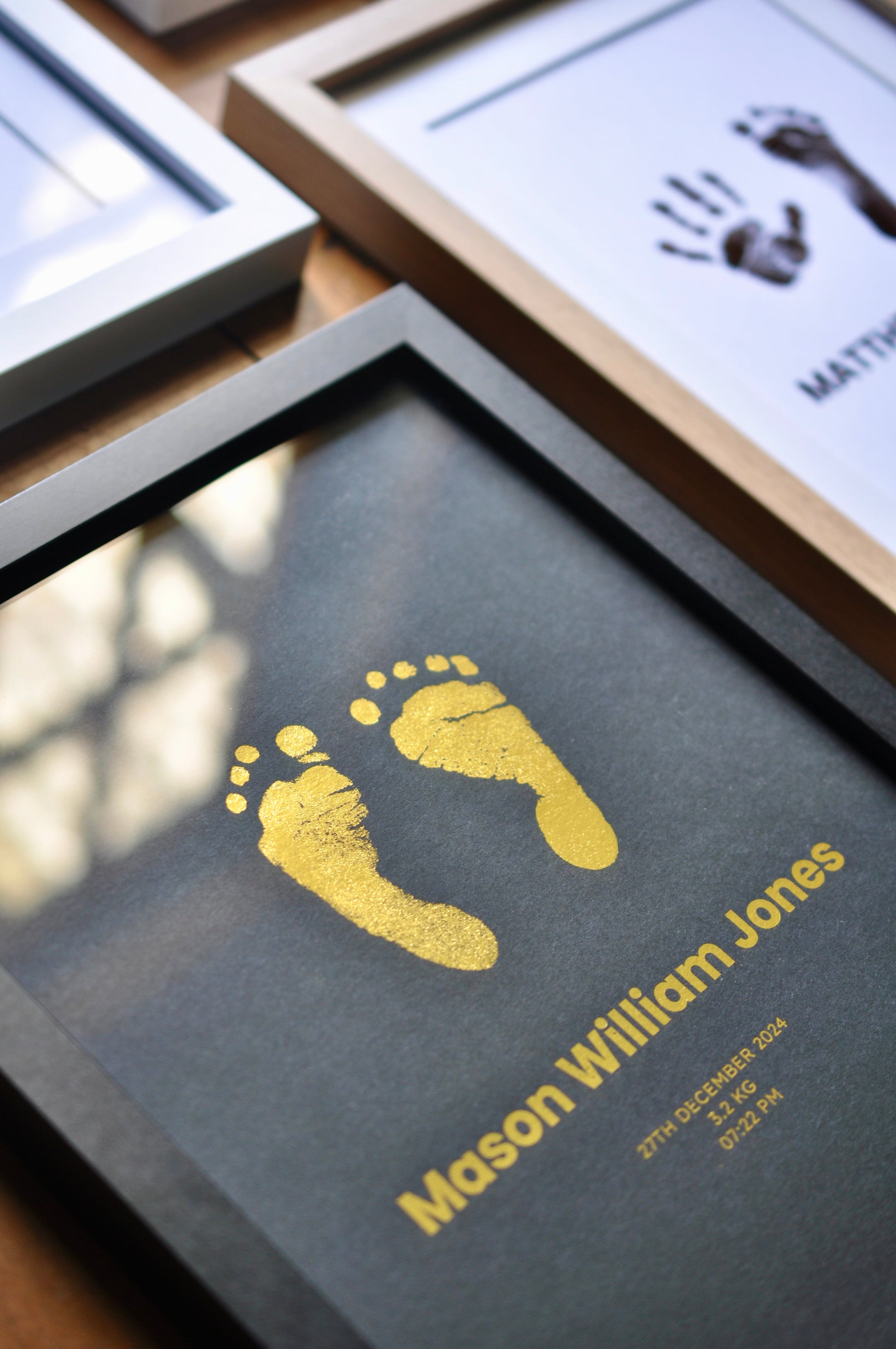 Framed baby footprint and handprint with personalized text on a wooden surface.