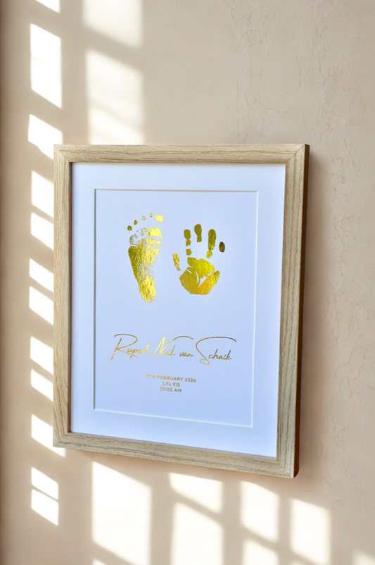 Framed artwork with gold footprints on a white background, mounted on a beige wall.