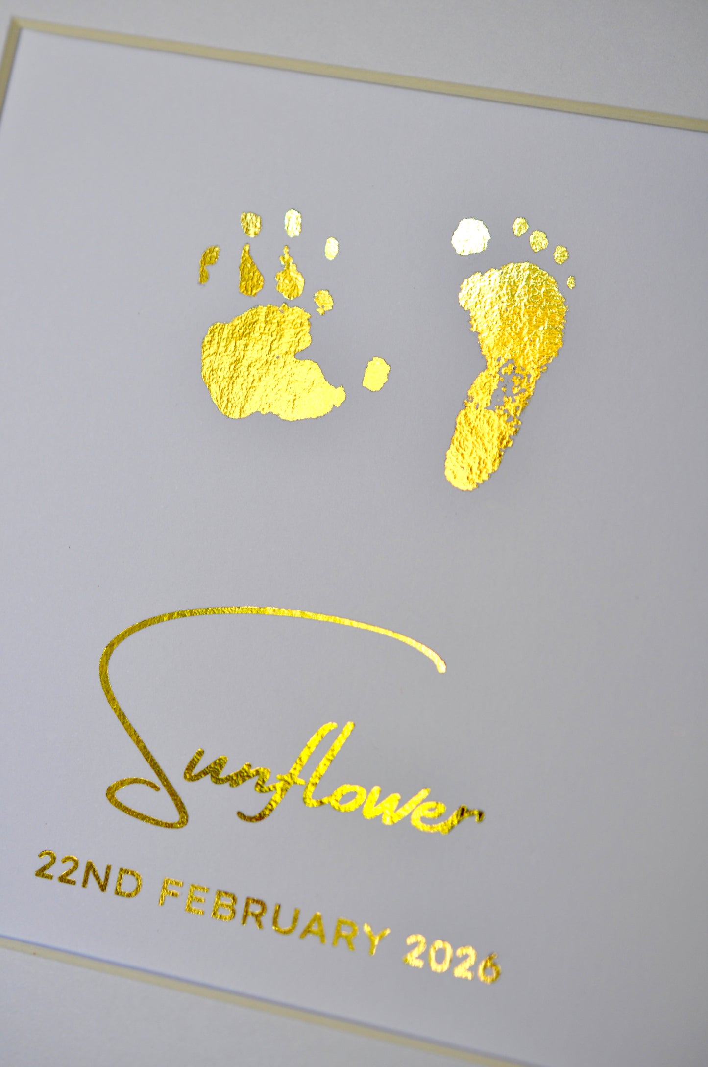 Gold foil baby footprints and handprints on a white card with 'Sunflower' and date printed.
