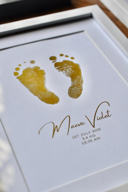 Framed gold baby footprints with name and birth details on a white background