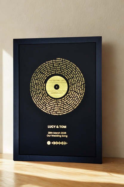 Framed artwork with gold text on a black background, displayed on a wooden surface.