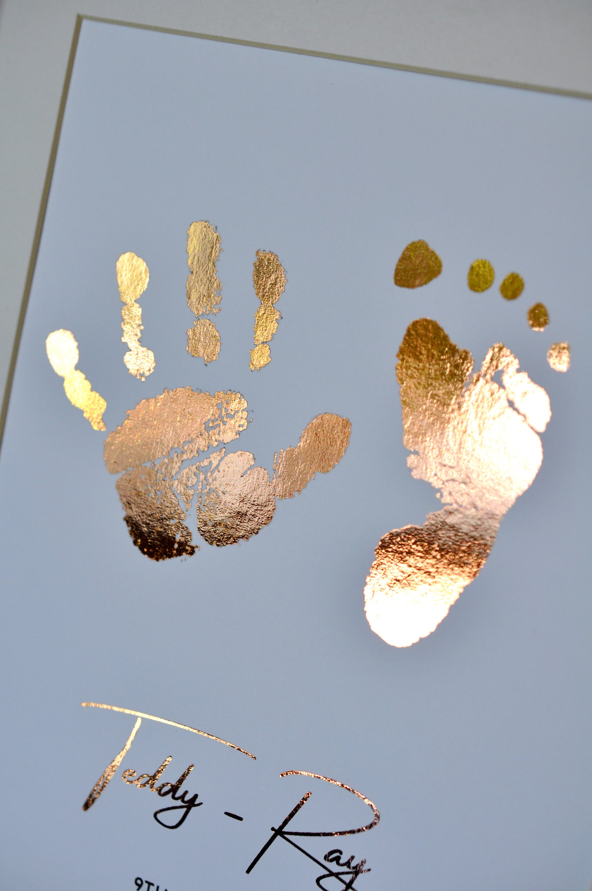 Rose gold hand and footprints on a white background with a signature at the bottom.