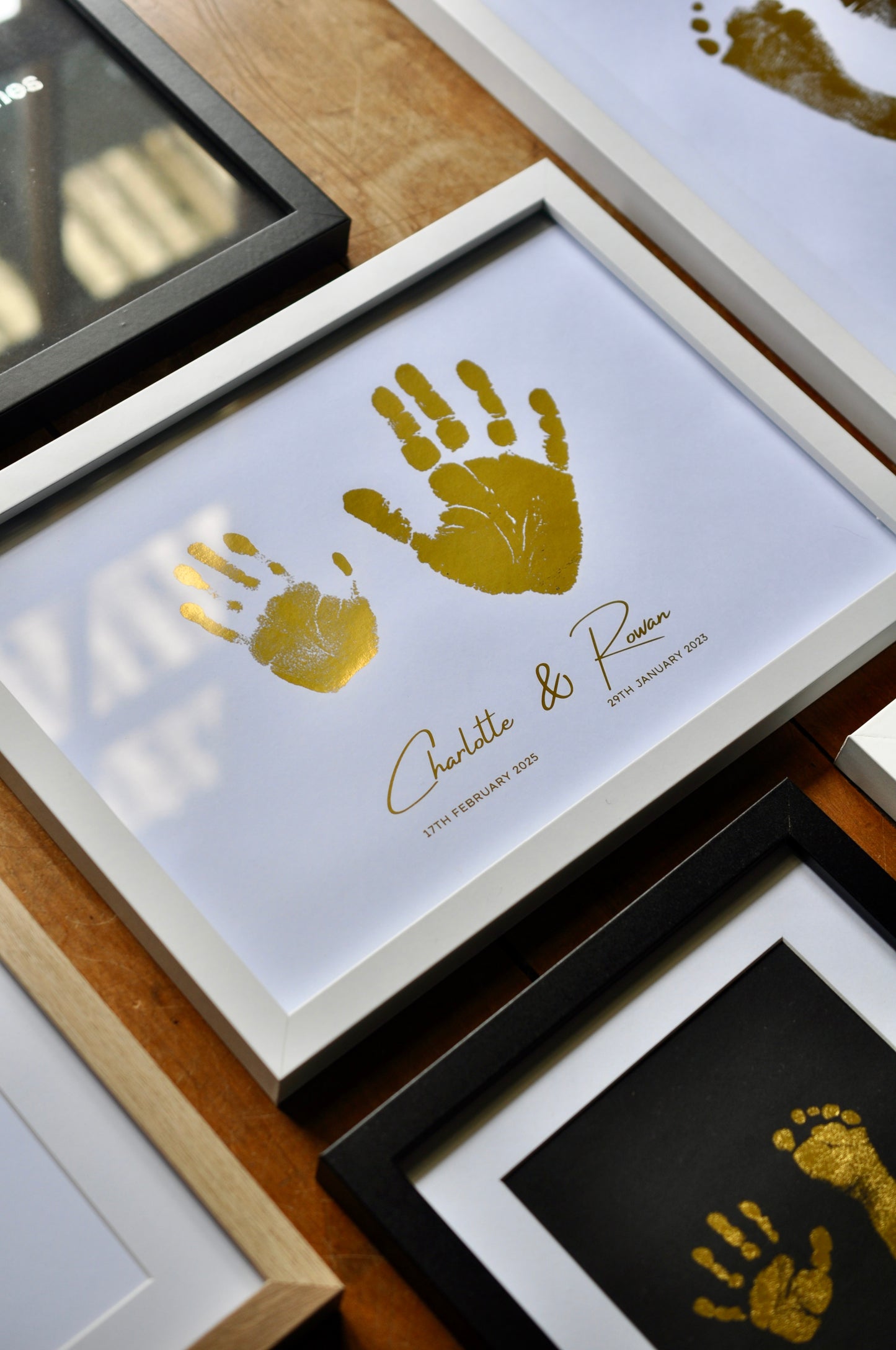 Framed gold handprints with names and dates on a wooden surface