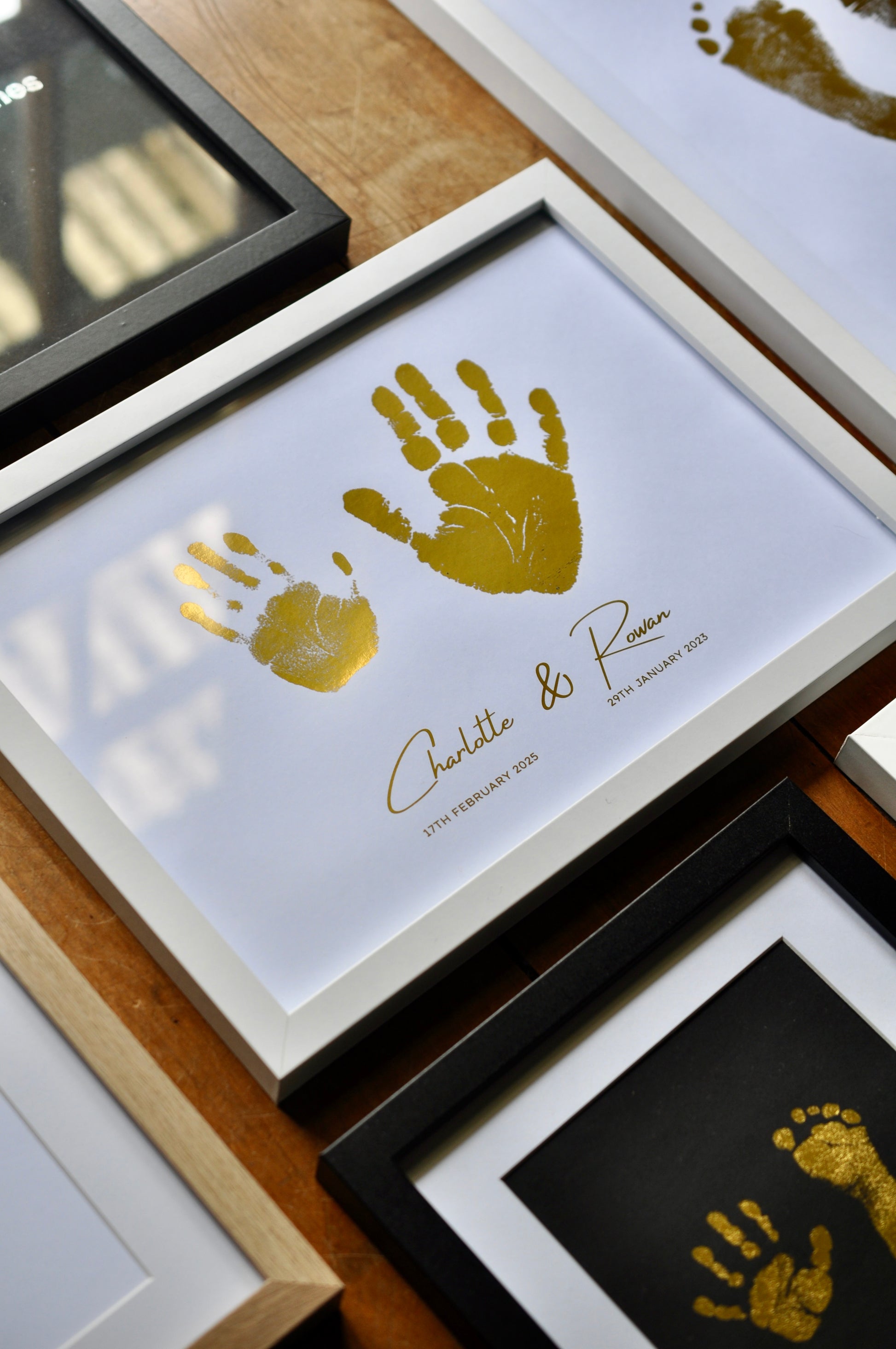 Framed gold handprints with names and dates on a wooden surface
