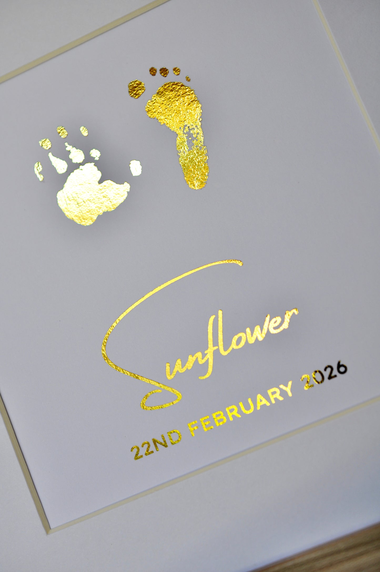 Gold foil baby footprints and handprints on a card with 'Sunflower' and '22nd February 2026' text.